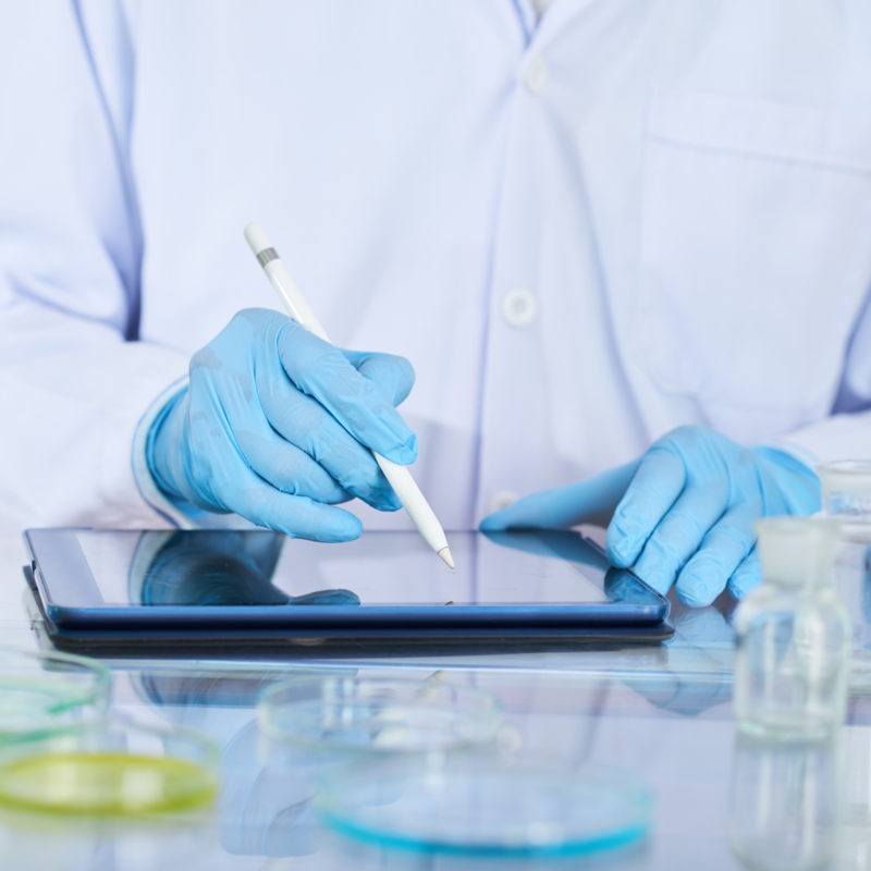 Close-up of chemist in protective glove using digital tablet in his work at lab